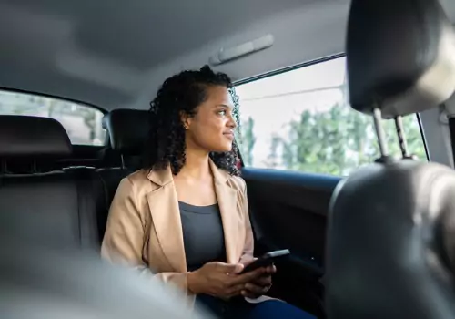 A woman smiles from the back of a cab while holding her phone. If you're asking "Does Peoria Have a Taxi Service" call Curt's Transportation Services today.