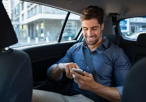 A man smiles while reading his phone in the back of a car from Curt's Transportation Services, which offers Taxis in Tazewell County IL