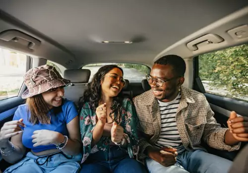 A group of three friends look at each other and laugh while riding in a cab from Curt's Transportation Services, which offers Taxi Service in Peoria County IL